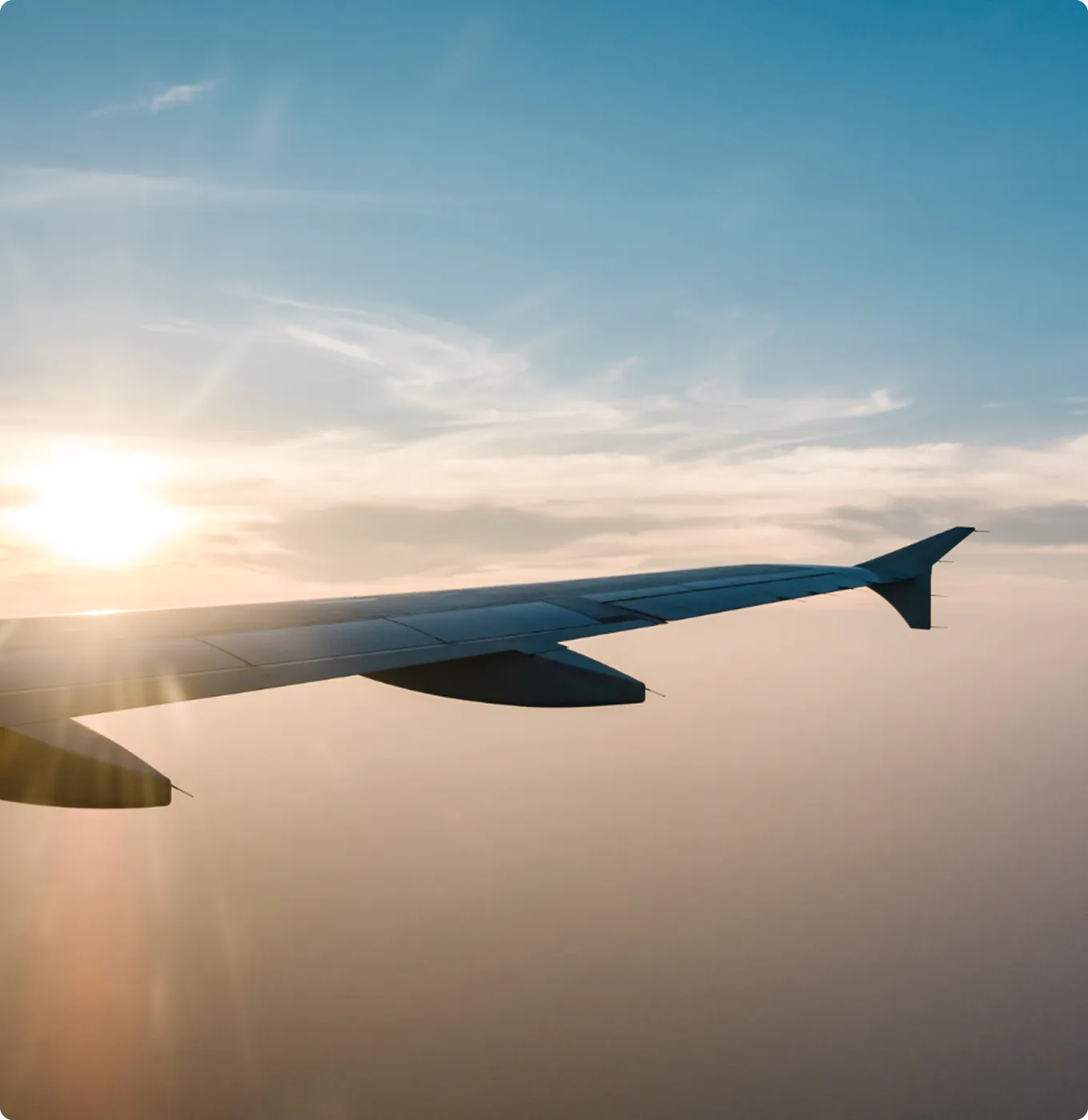 Airplane wing in flight above the clouds during a golden sunset.